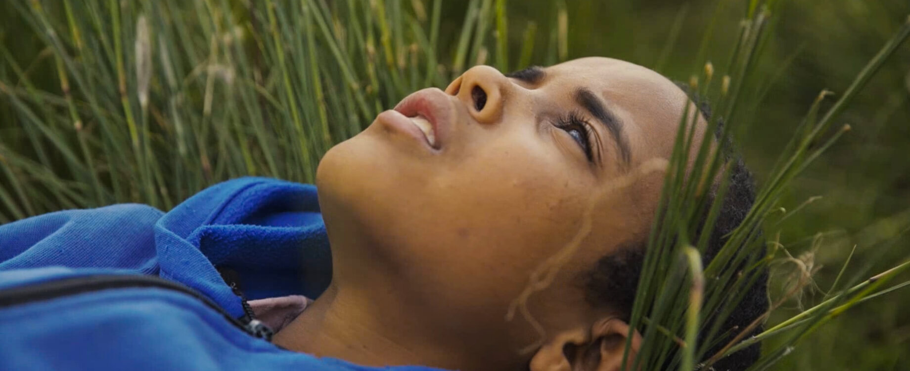 A young boy lying in the grass looks up at the sky.